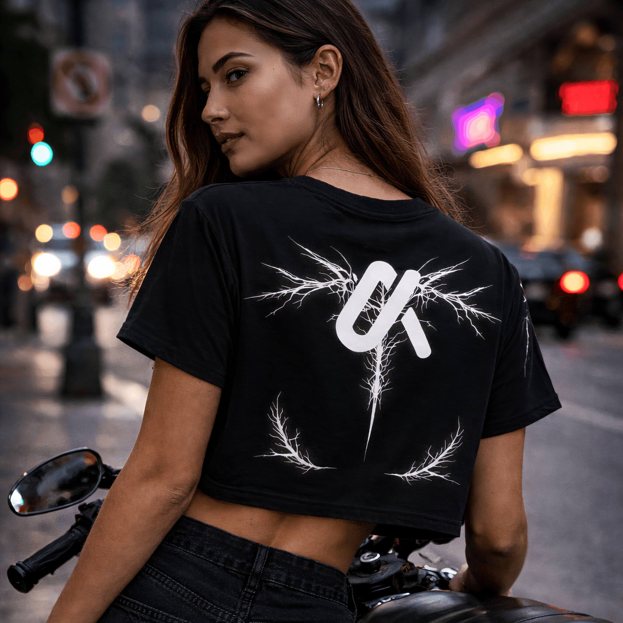 Woman leaning on a motorcycle wearing the LUMA Graphic Crop Tee, back graphic visible
