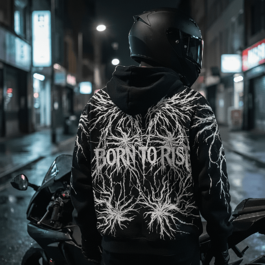 Rider wearing the LUMA Born to Rise hoodie on a city street at night beside a motorcycle