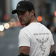 Man wearing the LUMA Ride After Dark Phoenix t-shirt and cap, close-up back view, city lights at night