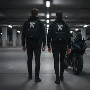 Two people wearing LUMA Tribal Ram backpacks walking toward a motorcycle in a parking garage