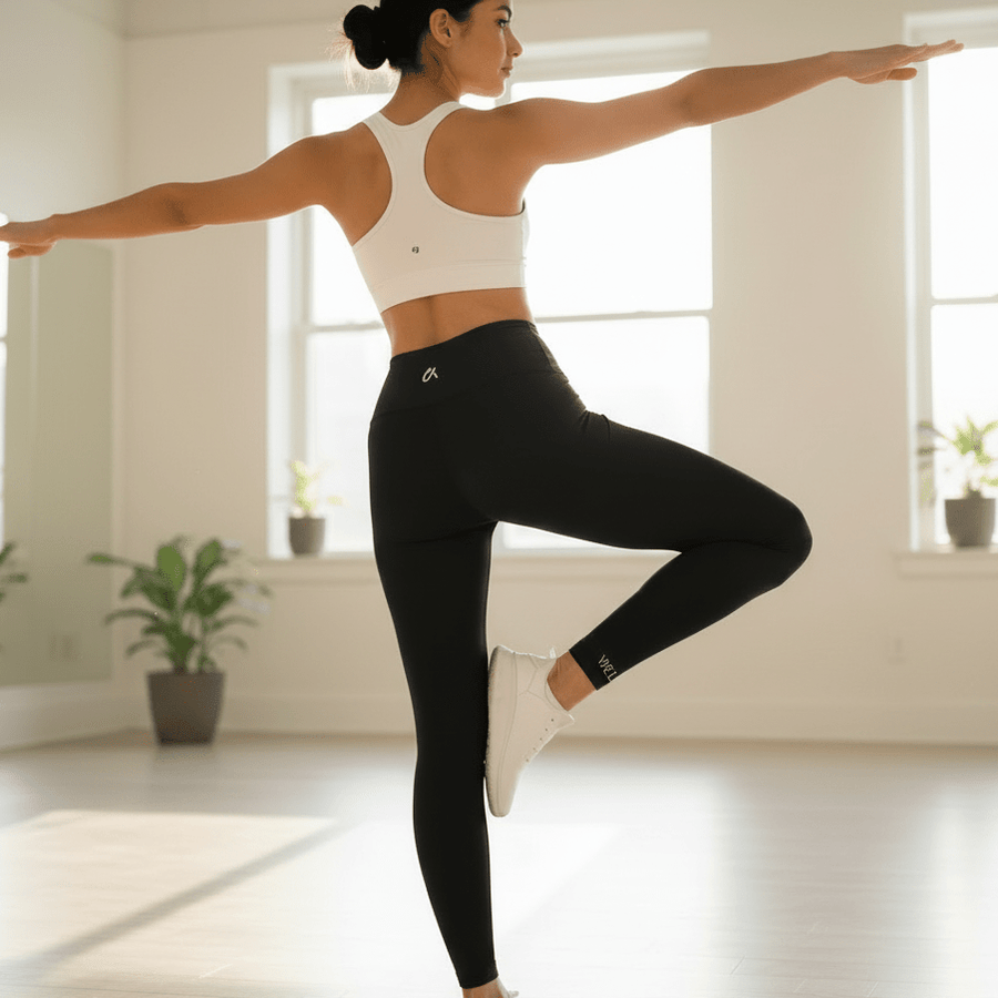 Woman in black high-waisted leggings doing a yoga balance pose in a studio