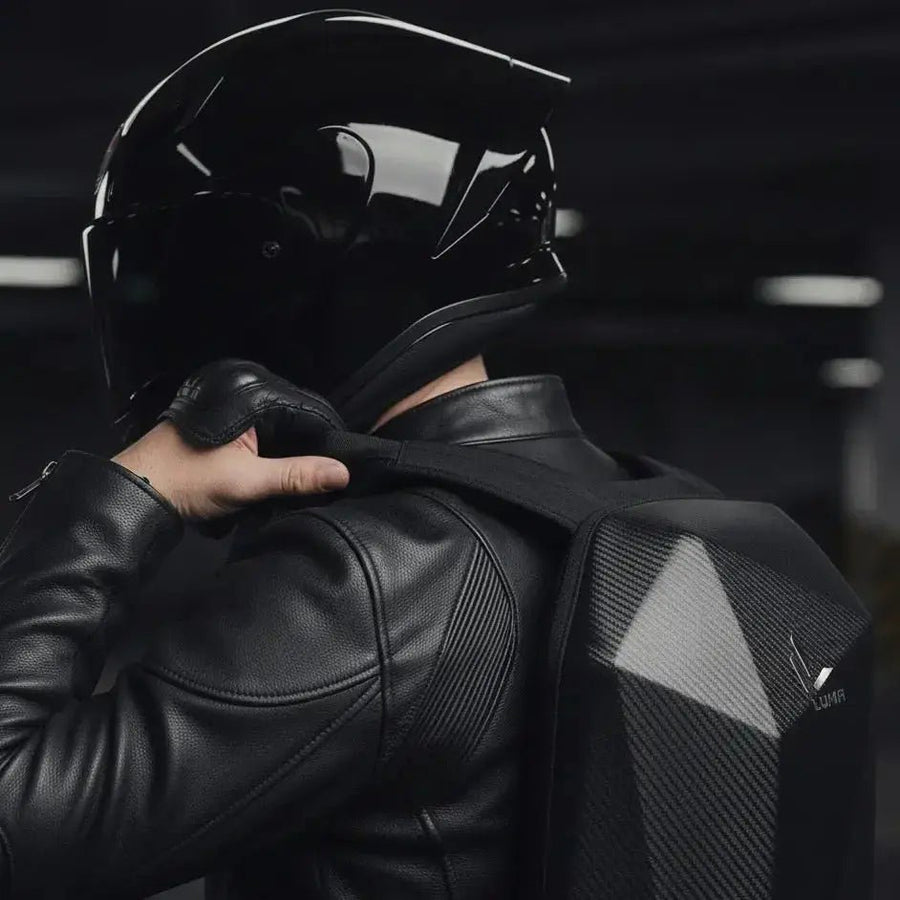 Close-up of rider adjusting the LUMA CarbonRide backpack strap while wearing a motorcycle helmet