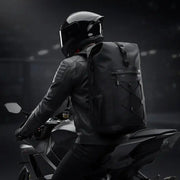 Motorcyclist riding a sportbike wearing the black LUMA AquaRider waterproof backpack, rear view