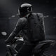 Motorcyclist riding a sportbike wearing the black LUMA AquaRider waterproof backpack, rear view