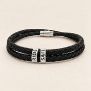 Black braided leather bracelet with magnetic clasp and two engraved steel beads RIDE SAFE on a light background
