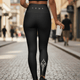 Woman walking a city street wearing LUMA black high-waisted leggings, back view showing leg graphic