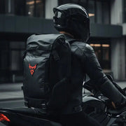Motorcyclist walking through the city wearing the LUMA MotoPack Pro backpack, red logo detail, rear view